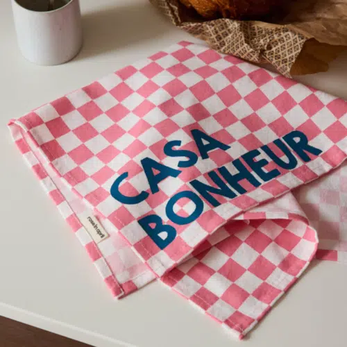 Set de 2 serviettes de table en coton, motif damier rose, message “Casa Bonheur” en situation sur une table dressée pour un repas familial