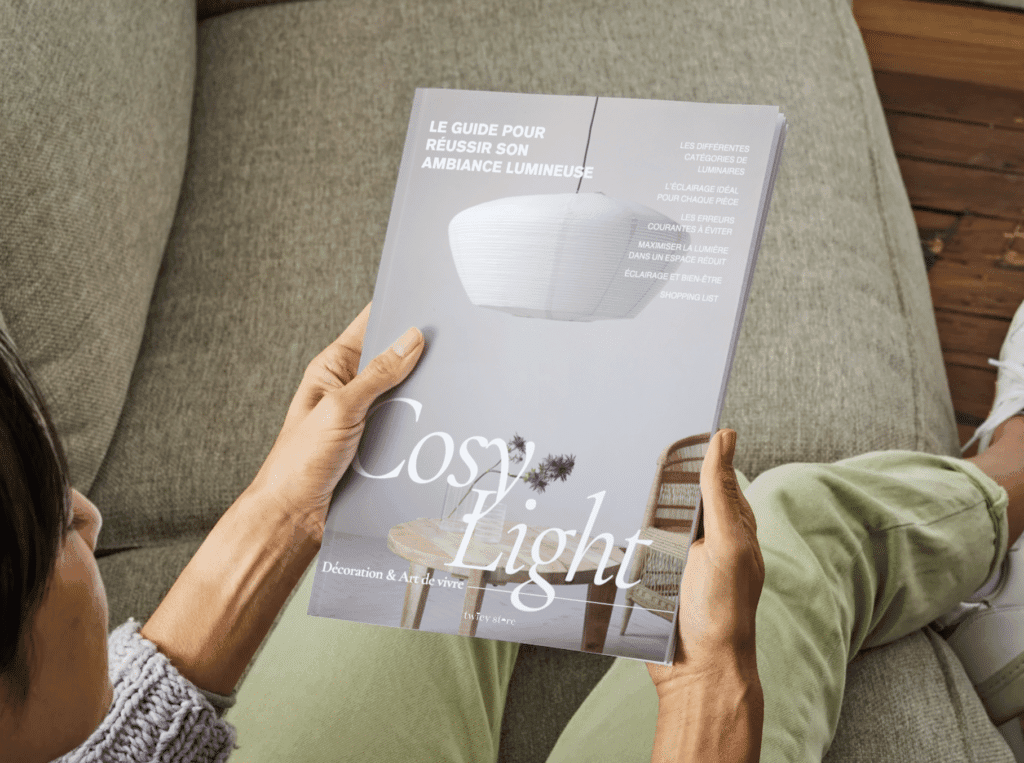 Cosy Light guide gratuit à télécharger pour réussir son ambiance lumineuse édité par Twicy Store tenu entre les mains d'une lectrice assise dans un salon