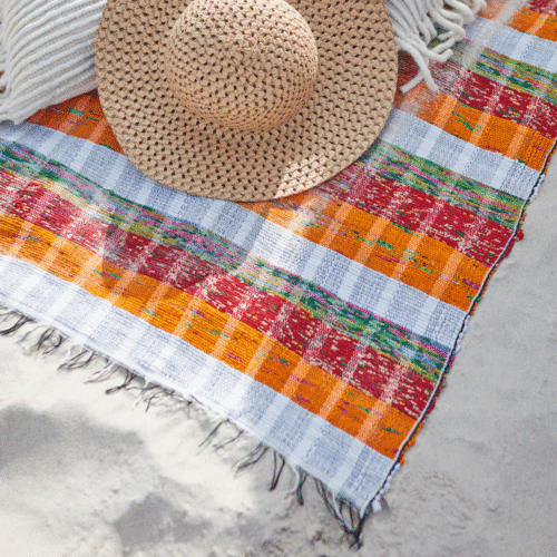 Couverture de pique-nique "Solveig" - Twicy Store posée sur le sable avec un chapeau de paille