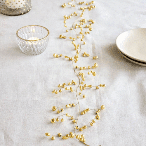 Guirlande de petites clochettes - Twicy Store disposée au centre d'une table de repas sur une nappe blanche