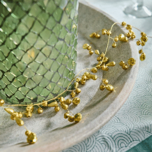 Guirlande de petites clochettes - Twicy Store disposée devant un photophore en mosaïque vert