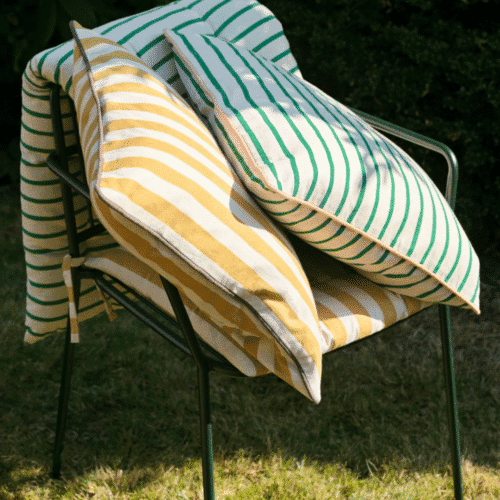 Housse de coussin en coton à rayures jaunes "Franca" - Twicy Store disposé sur une chaise en métal à l'extérieur