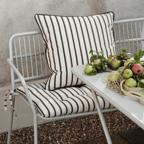 Housse de coussin en coton à rayures brun “Franca” - Twicy Store sur un banc en métal à l'extérieur devant une table de repas